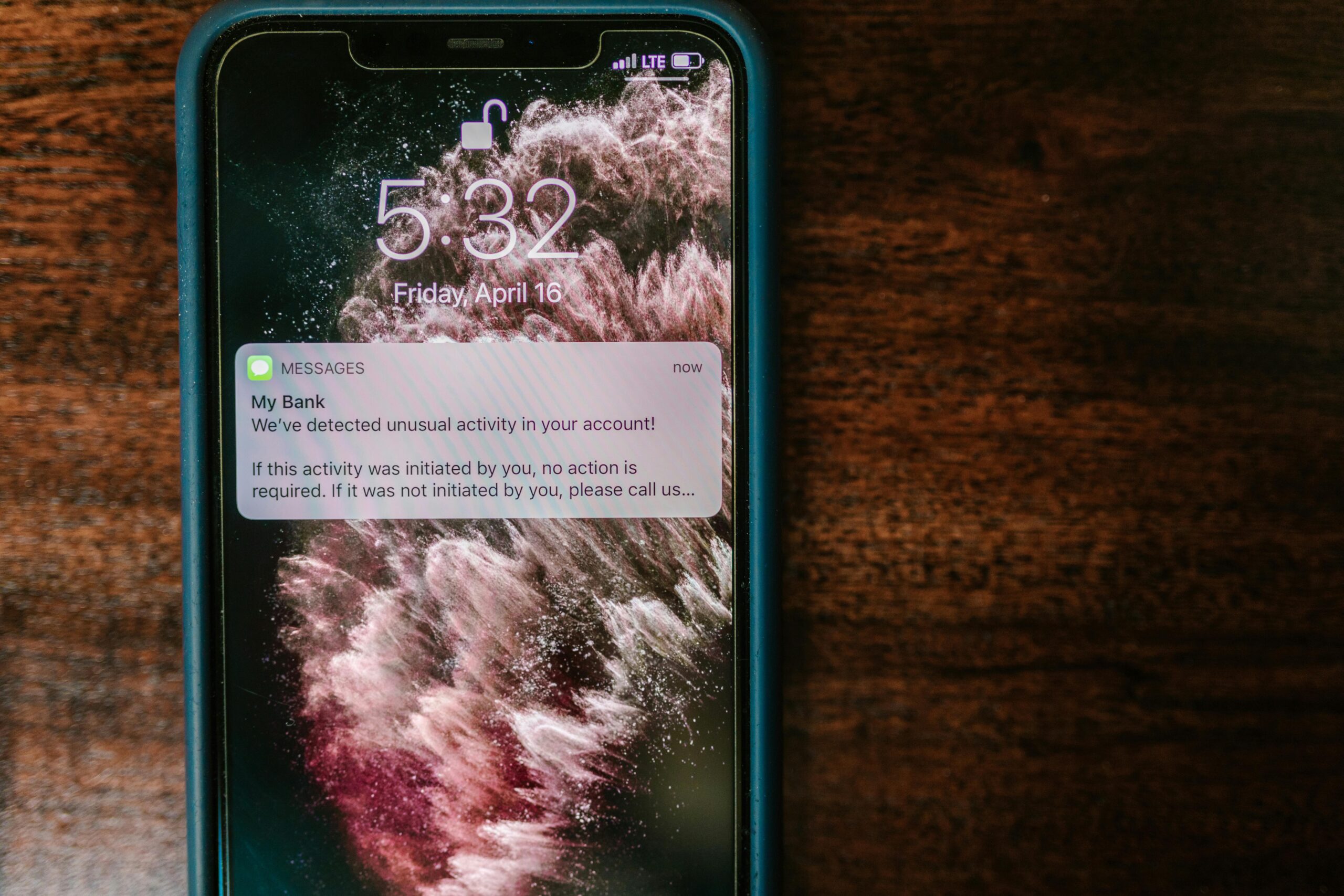 Close-up of a smartphone displaying a bank alert notification on a wooden table.